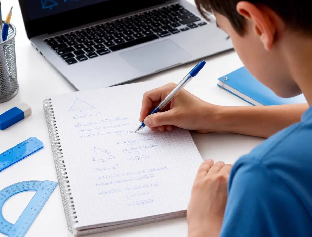 A student working through Math problems beside a laptop